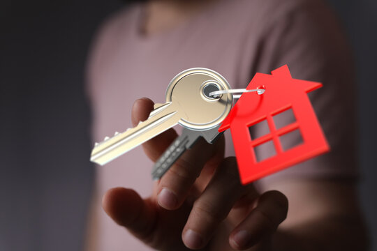 Close-up of a hand holding house keys and a red house-shaped tag. Illustrating home ownership, mortgage, or property investment. A symbol of sec