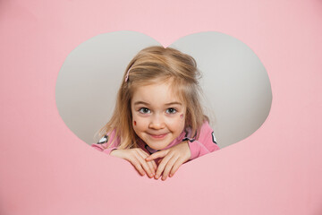Child peeking through heart-shaped cutout with smile on face indoors