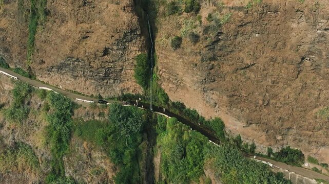 Aerial drone footage of famous Angel Falls of Madeira (Cascata dos Anjos), unique waterfall flowing directly over a coastal road. Filmed on a sunny day, clear water cascades down volcanic cliffs