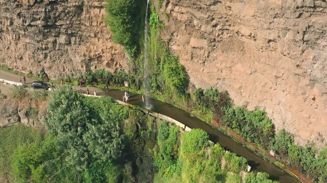 Aerial drone footage of famous Angel Falls of Madeira (Cascata dos Anjos), unique waterfall flowing directly over a coastal road. Filmed on a sunny day, clear water cascades down volcanic cliffs