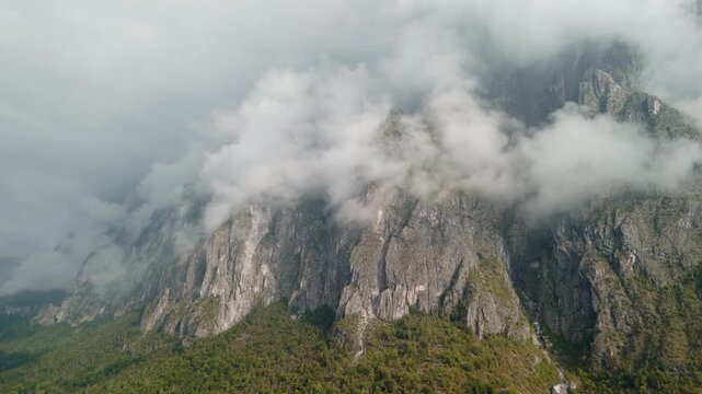 Aerial drone flying forward toward high Dolomite mountains with deep hanging clouds