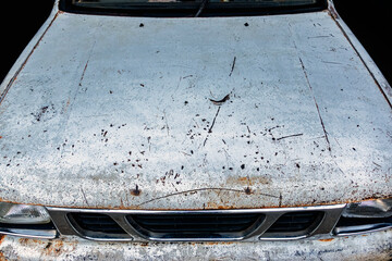 Old rusty white car with damaged paintwork on bumper and hood. Rusted ,cracked and peeling clear coat on top of vehicle bonnet hood. Car body deterioration and rust. Fragment of car hood with rust.
