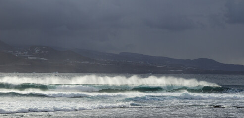 Gran Canaria, view towards Atlantic ocean from El Confital beach on the edge of Las Palmas de Gran Canaria, big waves crushing, rain in the mountains
