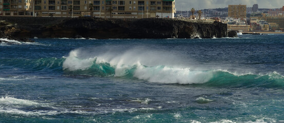 Gran Canaria, view towards Atlantic ocean from El Confital beach on the edge of Las Palmas de Gran Canaria, big waves crushing, rain in the mountains
