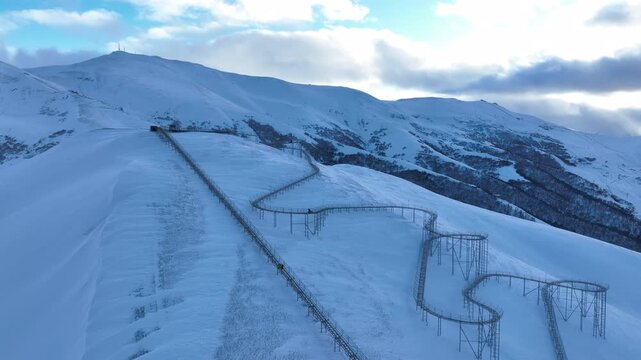 Drone view of a bobsled mountain coaster winding through the snow-covered Caucasus mountains in Bakuriani resort, featuring people enjoying the winter attraction.