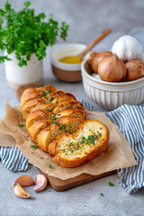 Freshly baked garlic bread, sliced and garnished with herbs, served on a wooden board with garlic cloves, olive oil, and shallots in the background, showcasing delicious culinary presentation