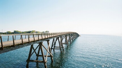 Obraz premium Wide shot of wooden pier extending over calm blue water. Serene coastal landscape with clear sky and distant shoreline. Tranquil seaside view capturing peaceful ocean horizon at sunrise.