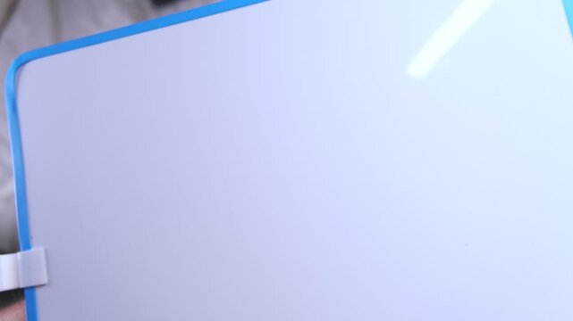 Person's hand using a cloth to wipe the word wow off a small magnetic dry erase board