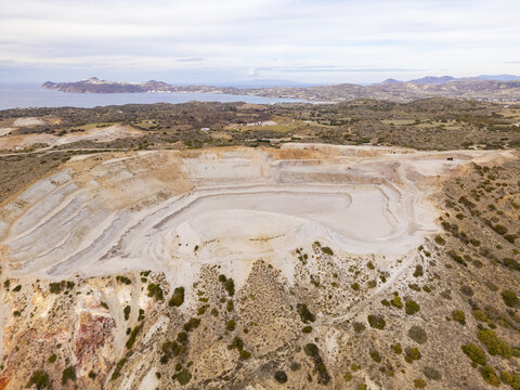 Aerial view of a vast, disused quarry pit carved into the earth, contrasting sharply with the distant sea and sky, Tsigrado beach, Milos, Greece.