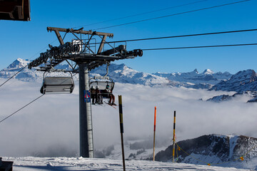 Ski resort with skiers riding a chairlift over a sea of clouds. Beautiful mountain scenery in the Sw