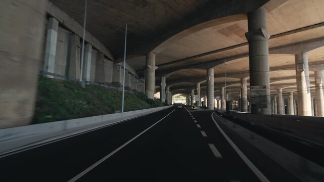 POV footage from a car driving under the massive concrete columns supporting runway Madeira Airport. Captures the scale and engineering of the airport infrastructure from a close, dynamic perspective