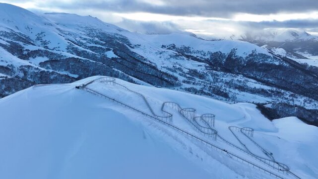 Drone view of a bobsled mountain coaster winding through the snow-covered Caucasus mountains in Bakuriani resort, featuring people enjoying the winter attraction.