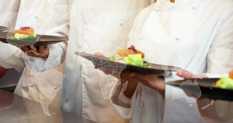 Presenting chefs in chef coats holding black plates with green garnish at pass counter, map overlay