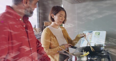 Stirring Chinese woman wearing mustard cardigan cooking in kitchen on gas stove, with wooden spoon
