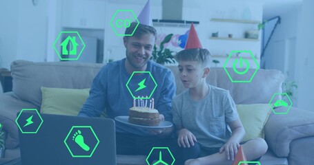 Smiling father-son wearing cone hats, holding cake, leaning blowing candles at home, green AR icons
