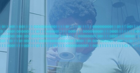 Sipping man in light tee looking out window at home, holding white mug beneath binary overlay