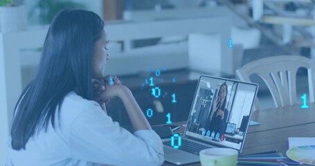 Leaning woman in white shirt attending remote call at wooden table, with laptop and color swatches
