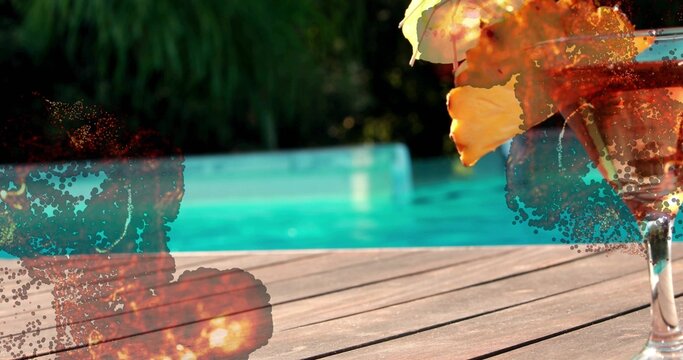 Stemmed cocktail glass sitting on deck by turquoise pool, yellow petal, paint splatter, copy space