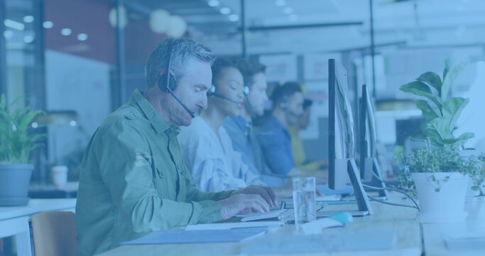 Typing man wearing green shirt and headset at office desk with monitors and glass, copy space - Powered by Adobe