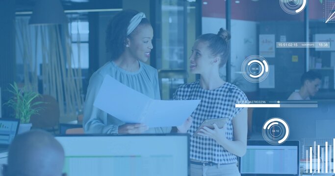 Reviewing two women in office attire holding large document and tablet in office with HUD overlays - Powered by Adobe