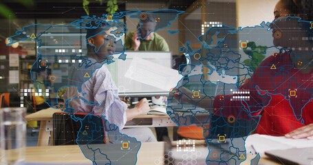 Collaborating team wearing green and red tops reviewing documents on desks with world-map overlay