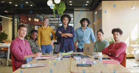 Gathering team wearing sweaters, shirts at wood table in office, showing open laptop and documents