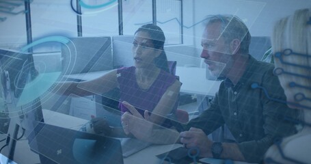 Pointing woman in sleeveless purple top leading meeting with two coworkers at office, with monitors