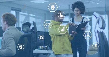 Presenting man in yellow hoodie pointing at tablet in open office, showing hexagon data overlays