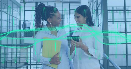 Talking coworkers in light blouses showing phone on office stairs, with yellow file and green data
