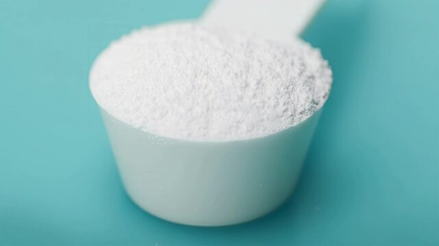 Close-up of a white protein supplement powder scoop on blue background, ideal for commercial fitness, nutrition, and health marketing visuals, featuring taurine, featuring arginine, featuring Glutamin