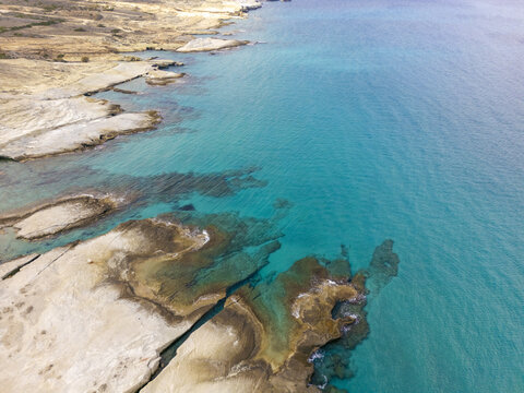 Aerial view of turquoise waters meet the rugged coastline, where light-colored rocks contrast with the deep blues of the sea, Paralia Mitikas, Milos, Greece.
