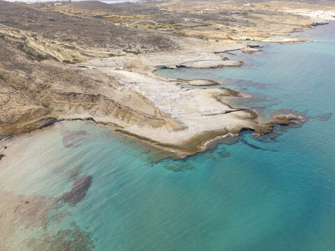 Aerial view of turquoise waters embracing the rugged coastline, where golden sands meet the horizon in a dance of light and shadow, Paralia Mitikas, Milos, Greece.