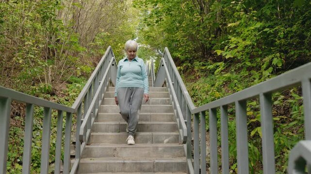 Elderly woman walking down outdoor stairs and feeling sudden knee pain