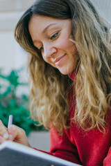 Young woman writing in a journal, smiling while focusing on her creative thoughts, expressing ideas with pen and paper, capturing inspiration and personal reflections