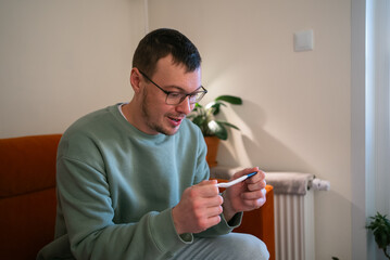 Man holding a pregnancy test stick, looking at the positive result with an expression of surprise and happiness, anticipating fatherhood and the arrival of a new family member