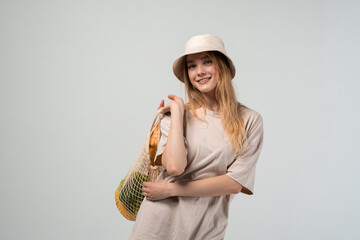 Young woman in bucket hat carrying reusable mesh shopping bag over shoulder, sustainable lifestyle and eco shopping concept