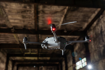 Grey drone maneuvering through an old industrial structure with rotating propellers and red status light visible on the battery compartment