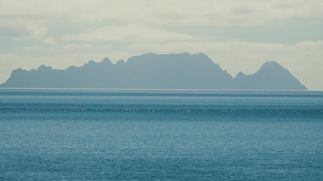 A telephoto shot of the distant silhouette of the Desertas Islands, captured from the parking area of Madeira Airport. The remote islands appear on the horizon approximately 35 kilometers away