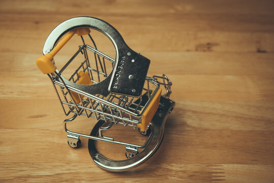 Handcuffs locked shopping cart on wooden table background copy space. Punishment for shoplifting, scammer in online shopping e-commerce and so on concept.