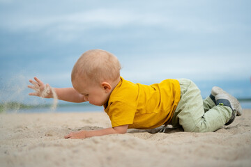 A curious baby in a bright yellow shirt explores the sand on a sunny beach, capturing the joy of discovery, play, and the simple pleasures of a day by the sea.
