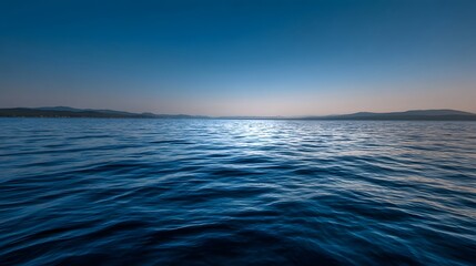 Obraz premium A serene expanse of deep blue water with gentle waves reflecting the light of a dusk sky
