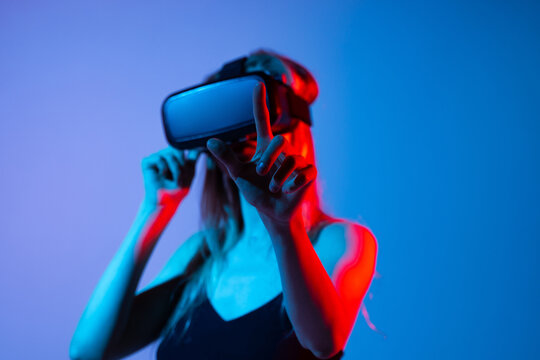 Female gamer using virtual reality headset and touching virtual interface in neon blue and red light, future technology concept - Powered by Adobe