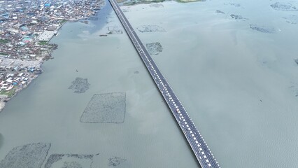 Aerial view of a long bridge cutting through the water, connecting landmasses under a hazy sky, Lagos, Lagos, Nigeria.