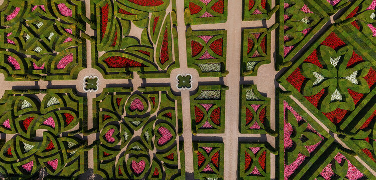 Aerial view of a meticulously designed garden with intricate patterns of vibrant red, pink, and green flora separated by beige pathways, Chaumont-sur-Loire, Centre-Val de Loire, France.