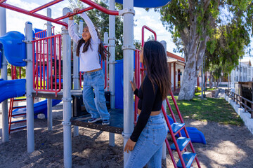 Young girl swinging on playground monkey bars with an adult woman watching