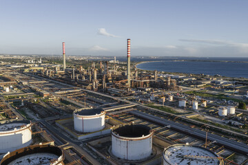 Aerial view of industrial complex with towering smokestacks reaching into the sky, contrasting against the serene blue coastline, Syracuse, Sicilia, Italy.