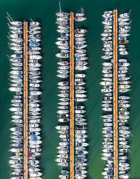 Aerial view of rows of boats nestled in their berths, a symphony of white against the deep teal harbor waters, Civitavecchia, Lazio, Italy.