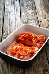 Raw seasoned chicken drumsticks in baking dish on wooden table	