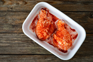 Raw seasoned chicken drumsticks in baking dish on wooden table. Top view