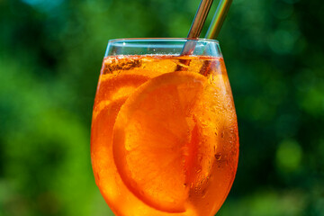Aperol spritz cocktail in wine glass on a nature background. Classic italian aperitif aperol spritz cocktail with orange and ice cubes. Closeup. Summer refreshing drink with sunlight